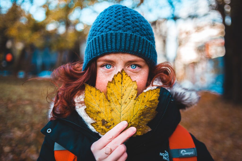 Girl in black knit cap holding yellow maple leaf